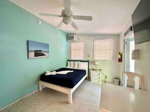 Un dormitorio con cama, ventilador de techo, aire acondicionado, mesita de noche, silla y ventana con persianas.