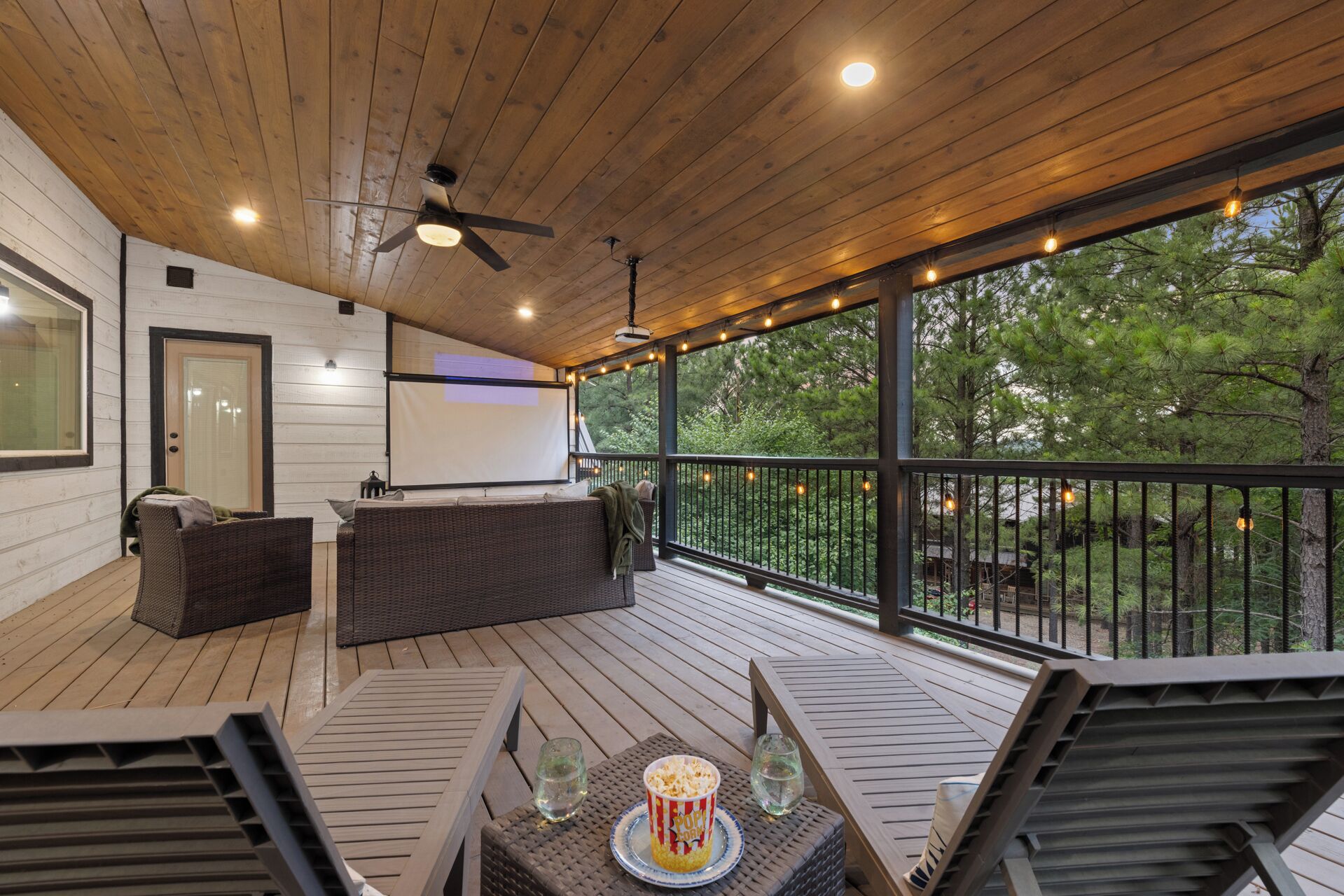 A covered outdoor deck with a ceiling fan, a projector screen, and a seating area with a table and chairs.