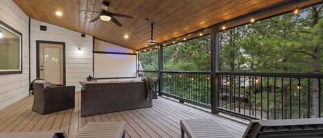 A covered outdoor deck with a ceiling fan, a projector screen, and a seating area with a table and chairs.