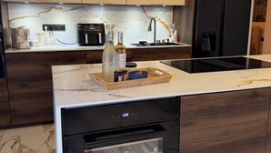Een moderne keuken met een marmeren aanrechtblad, ingebouwde apparatuur en een houten kast.
