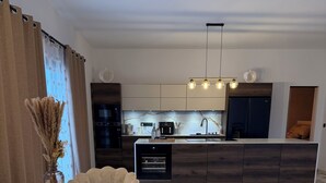 Een moderne keuken met een marmeren aanrechtblad, een eethoek met een marmeren tafel en gestoffeerde stoelen, en een zithoek met een bank.