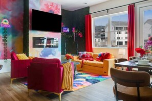 Ein modernes Wohnzimmer mit Flachbildfernseher, Kamin, einer Couch, einem Esstisch und einem großen Fenster mit Vorhängen.