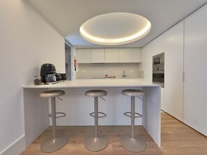A modern kitchen with a central island, bar stools, a coffee machine, and built-in appliances. - Bolhão Prime | Luxe 4BR + Garage (Porto)