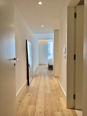 A hallway with wooden flooring, white walls, and a bed in the distance. - Bolhão Prime | Luxe 3BR + Garage (Porto)