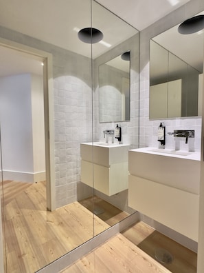 A modern bathroom with a glass partition, white tiled walls, and wooden flooring. - Bolhão Prime | Luxe 3BR + Garage (Porto)