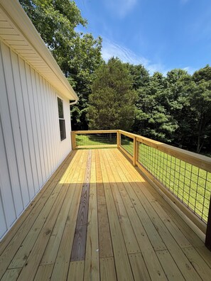 A wooden deck with a railing, a white building, and a grassy yard.