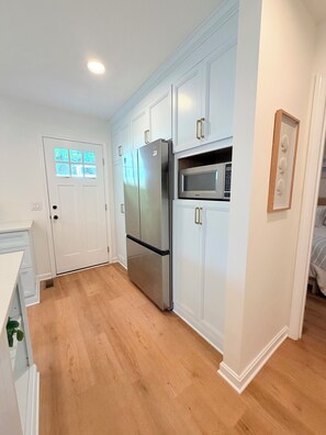 A kitchen with white cabinetry, a stainless steel refrigerator, a microwave, and a wooden floor.