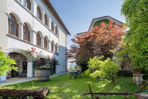 Une cour intĂ©rieure avec un bĂątiment dotĂ© de fenĂȘtres en arc de cercle et un jardin agrĂ©mentĂ© de plantes en pot et dâun arbre.