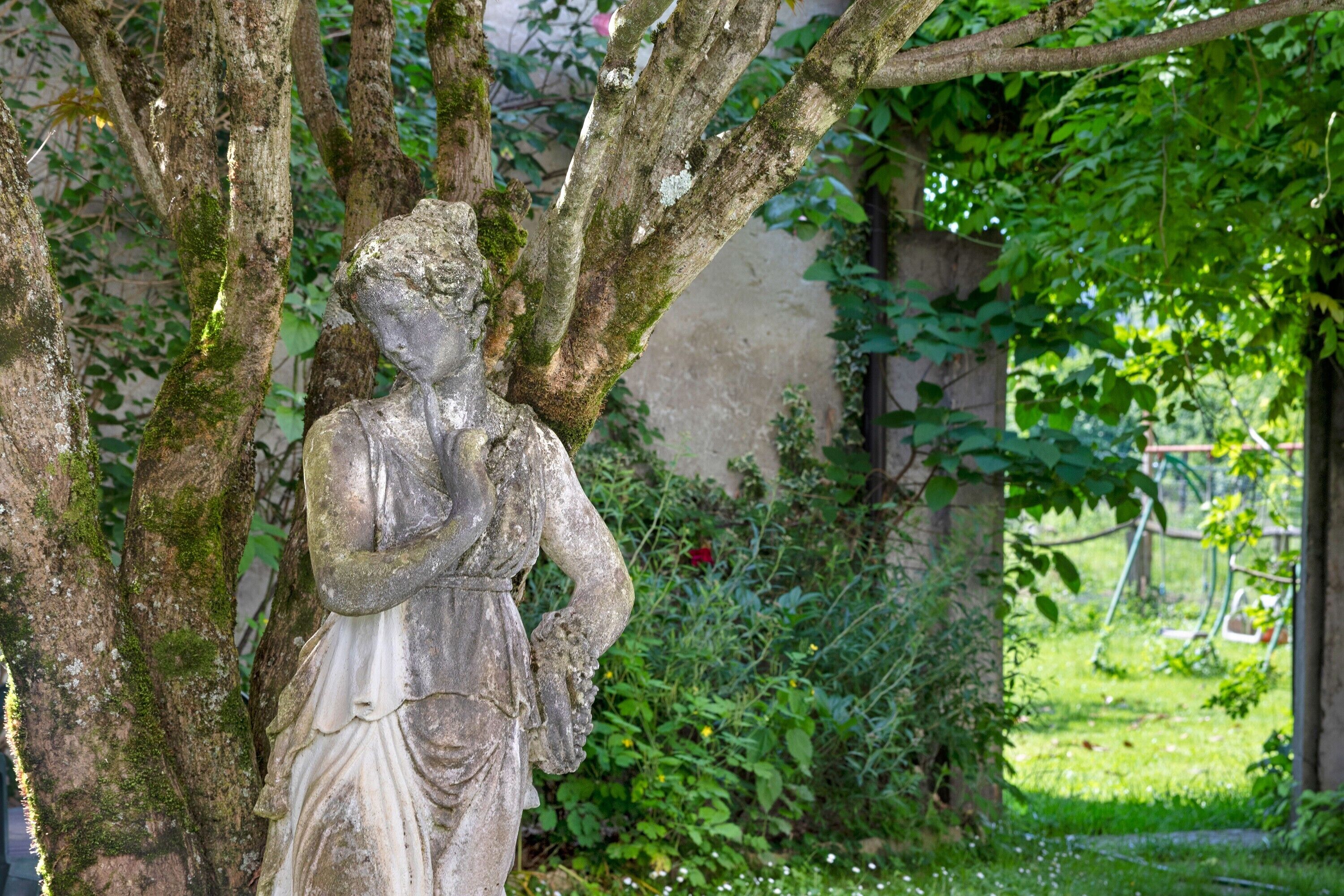 A stone statue of a woman in a garden with trees and greenery.