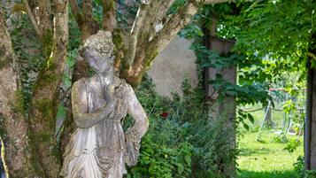 A stone statue of a woman in a garden with trees and greenery.