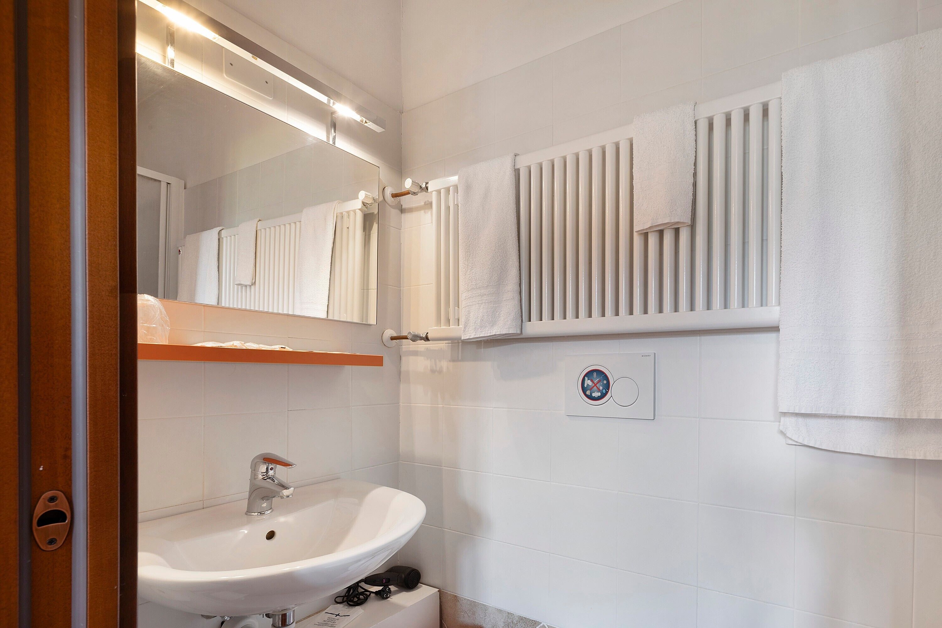 Un bagno con lavandino, specchio, porta asciugamani e un cartello appeso al muro.
