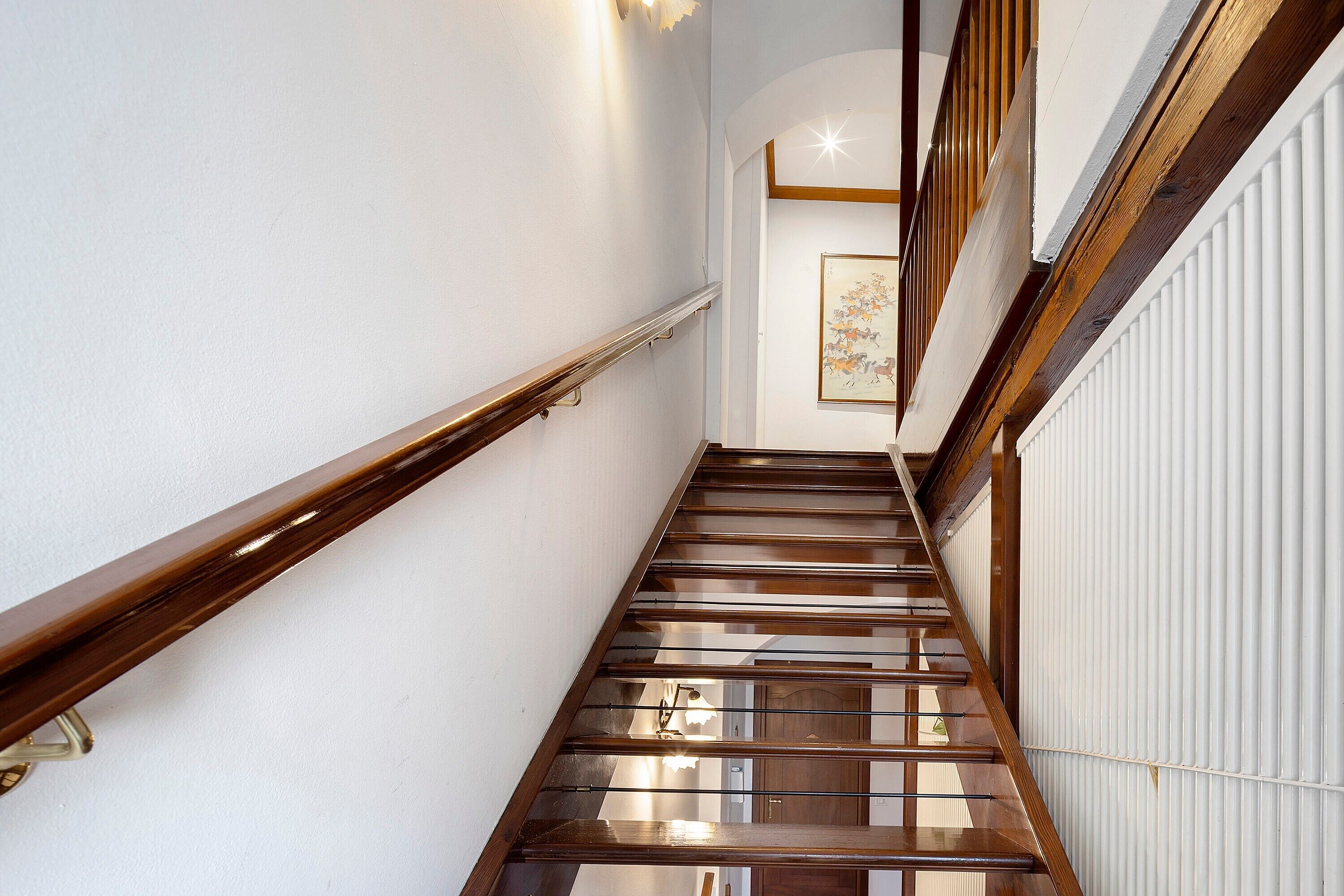 A wooden staircase with a handrail, white walls, and a framed artwork on the wall.