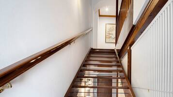 A wooden staircase with a handrail, white walls, and a framed artwork on the wall.