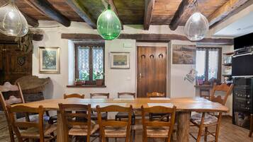 Un comedor rústico con una mesa y sillas de madera, techo de madera y lámparas de vidrio verde colgantes.