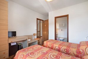 Ein Schlafzimmer mit Schreibtisch, Fernseher, zwei Betten mit gemusterten Bettbezügen, einem Spiegel und einem Kleiderschrank.