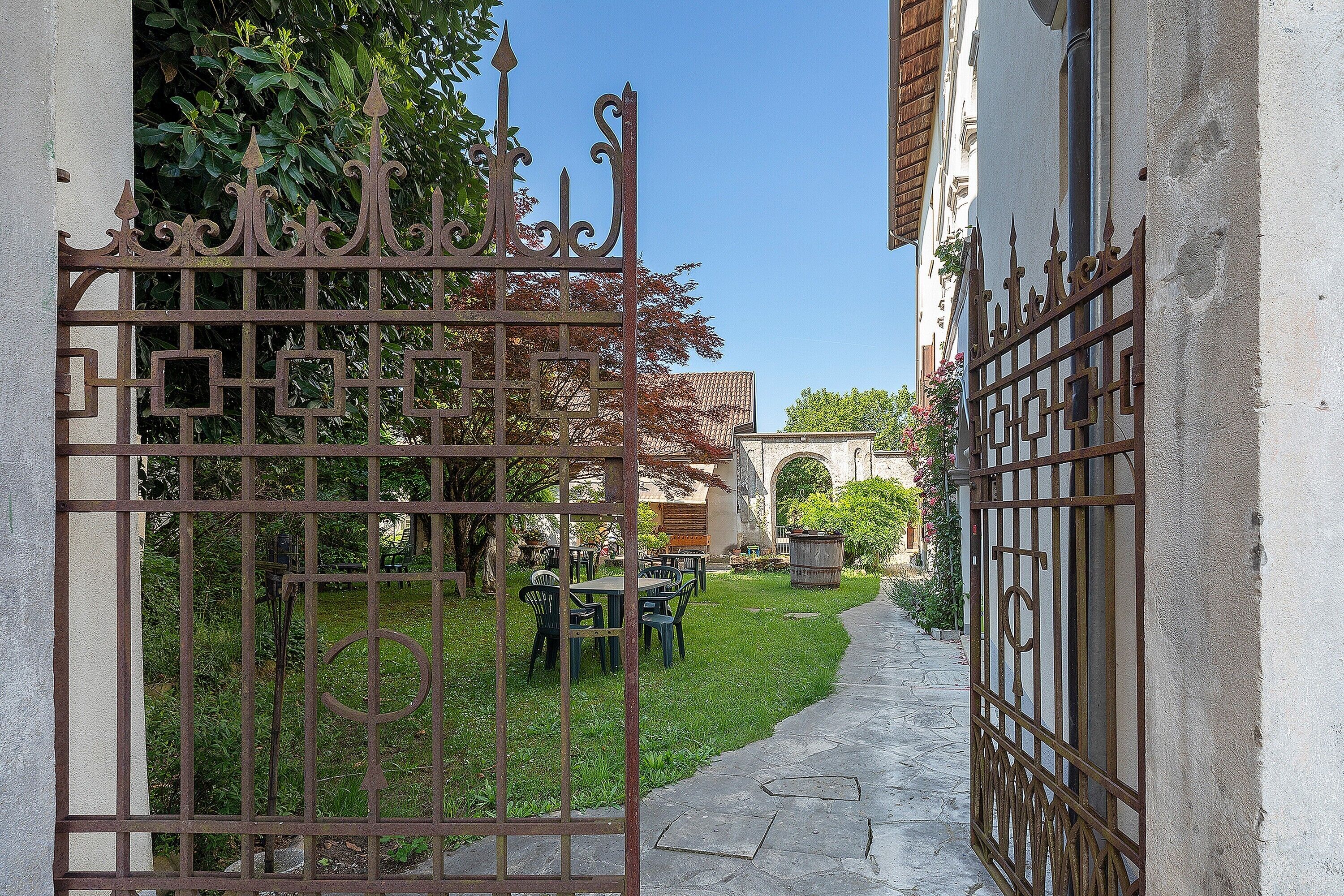 A gated courtyard with a stone pathway, outdoor seating, and greenery.