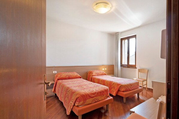 Ein Zimmer mit zwei Betten, Holzboden, Fenster und Deckenleuchte.