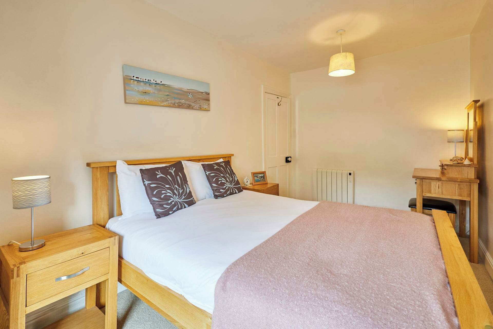 A bedroom with a bed, bedside tables, a lamp, a painting, a mirror, and a radiator.