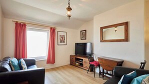 A living room with a sofa, a TV, a wooden cabinet, and a mirror. - Host & Stay | The Beach (Filey)
