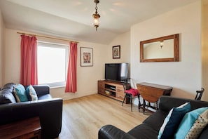A living room with a sofa, a TV, a wooden cabinet, and a mirror. - Host & Stay | The Beach (Filey)