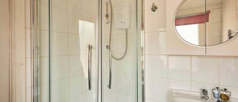 A bathroom with a glass-enclosed shower, a round mirror, and a white sink with toiletries.