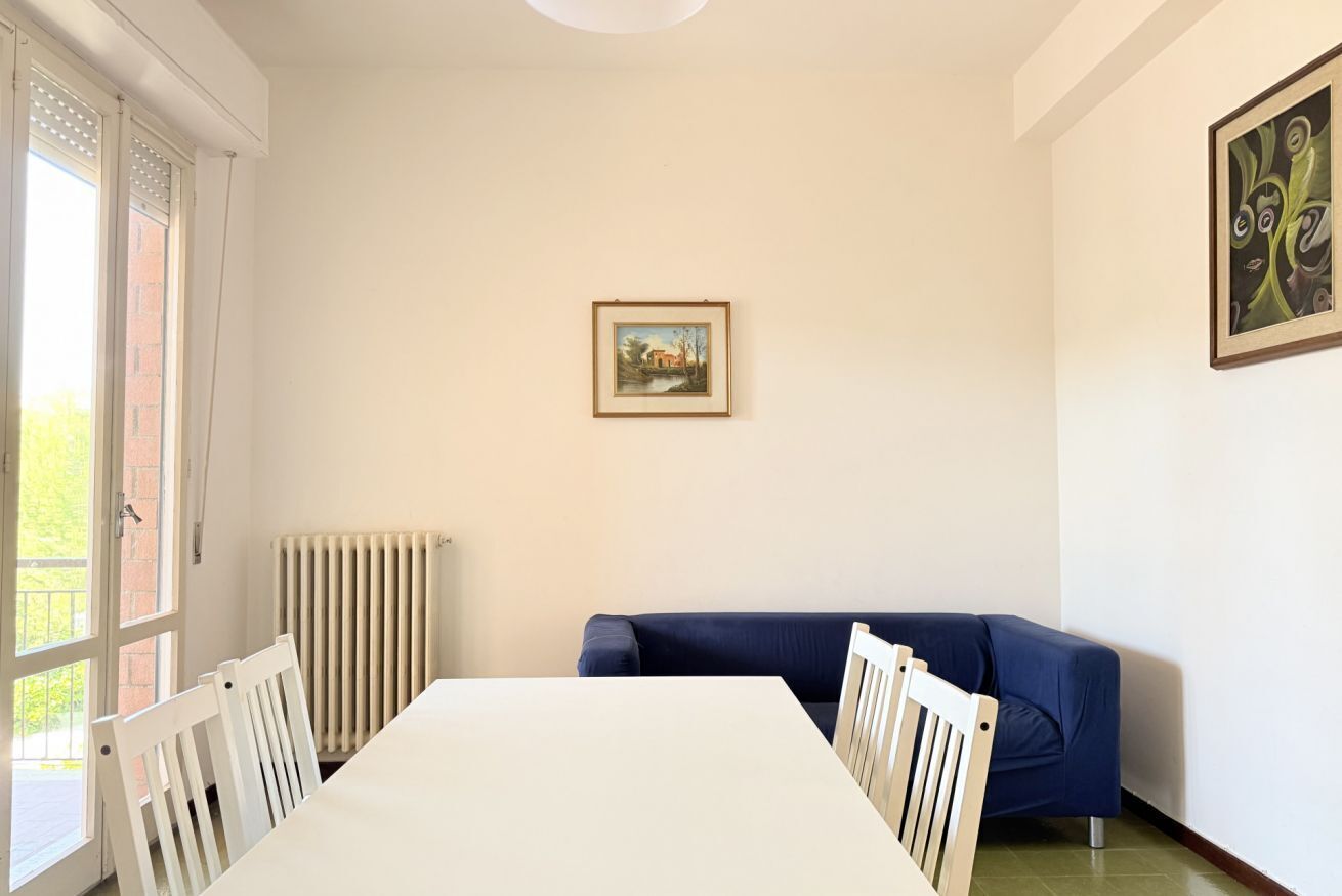A room with a dining table, chairs, a blue sofa, a radiator, and a framed picture on the wall.