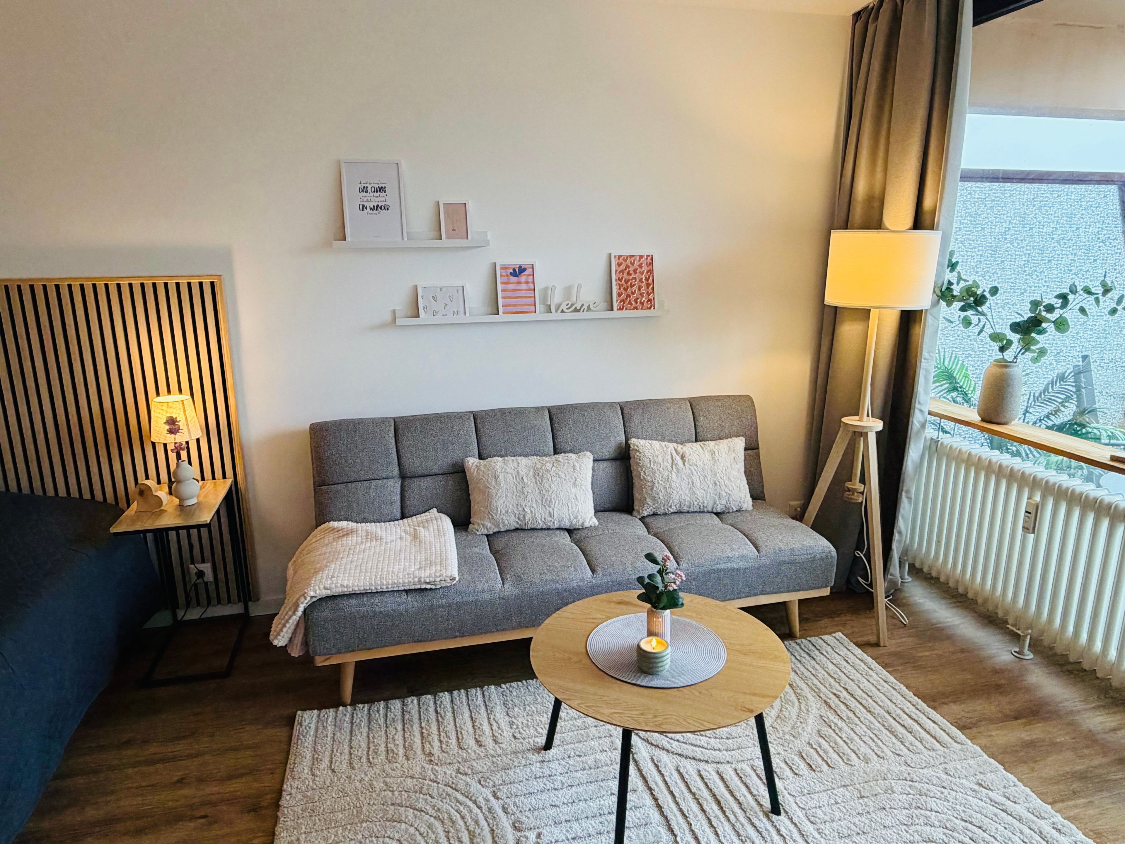 A modern living room with a grey sofa, a round wooden coffee table, and a small side table with a lamp.