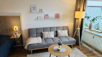 A modern living room with a grey sofa, a round wooden coffee table, and a small side table with a lamp.