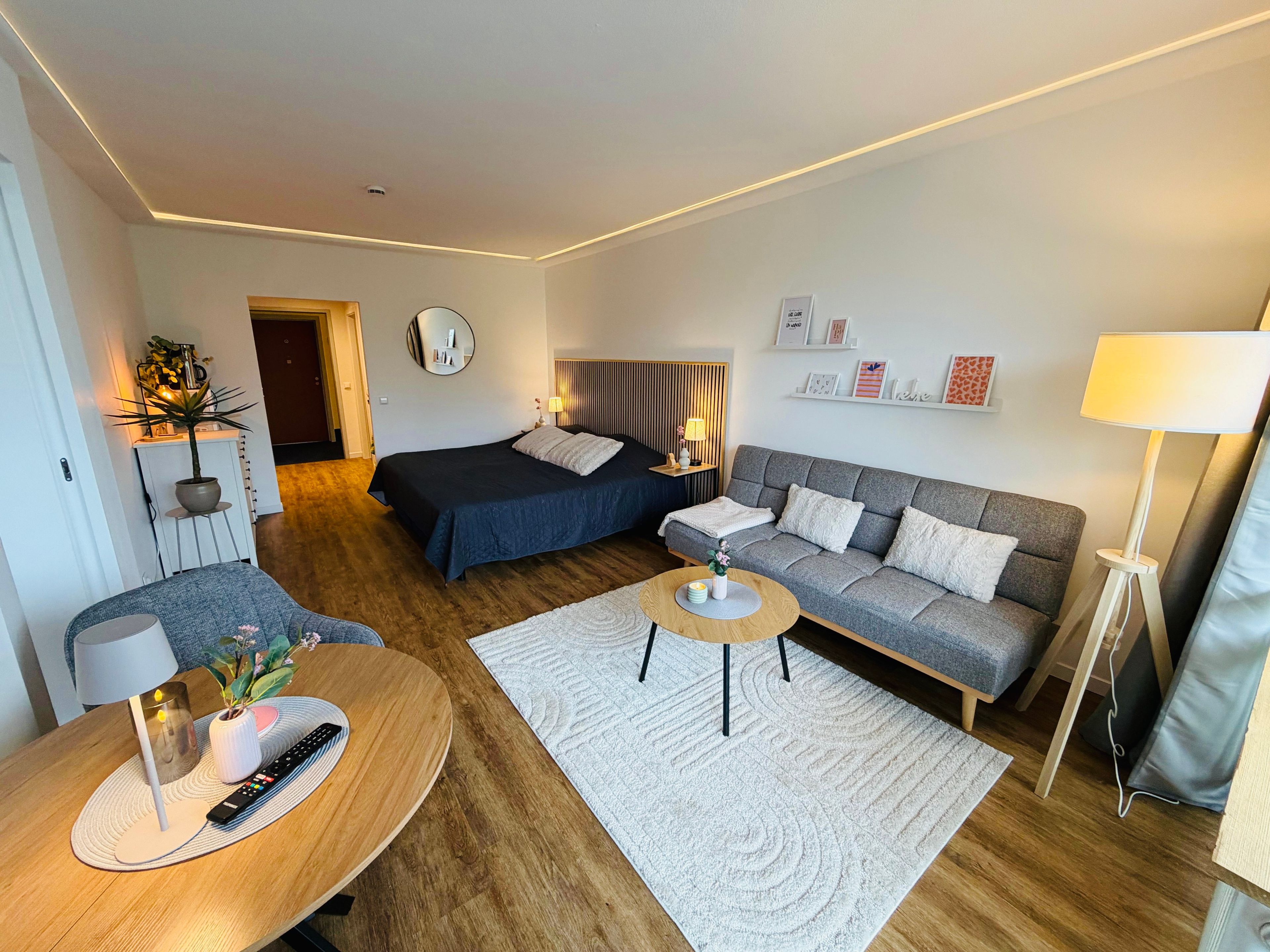 A modern hotel room with a bed, sofa, and a dining area.