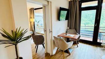 Een moderne kamer met een eethoek, een aan de muur bevestigde televisie en uitzicht op het groen door een groot raam.
