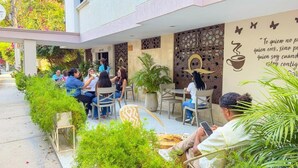 An outdoor seating area with tables and chairs, surrounded by greenery and a decorative wall with a quote. - HOTEL VALLADOLID (Santa Marta)