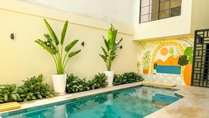 A swimming pool with potted plants, a tiled floor, and a decorative wall with a sun and palm design. - HOTEL VALLADOLID (Santa Marta)