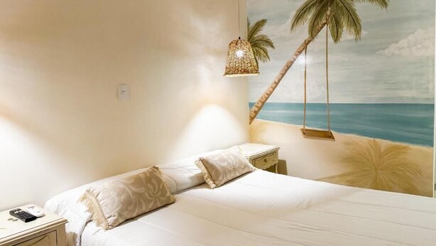 A bedroom with a bed, a nightstand, a lamp, and a wall mural of a beach scene. - HOTEL VALLADOLID (Santa Marta)