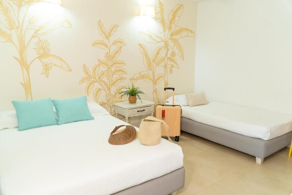 A hotel room with two beds, a nightstand, a suitcase, and a potted plant.