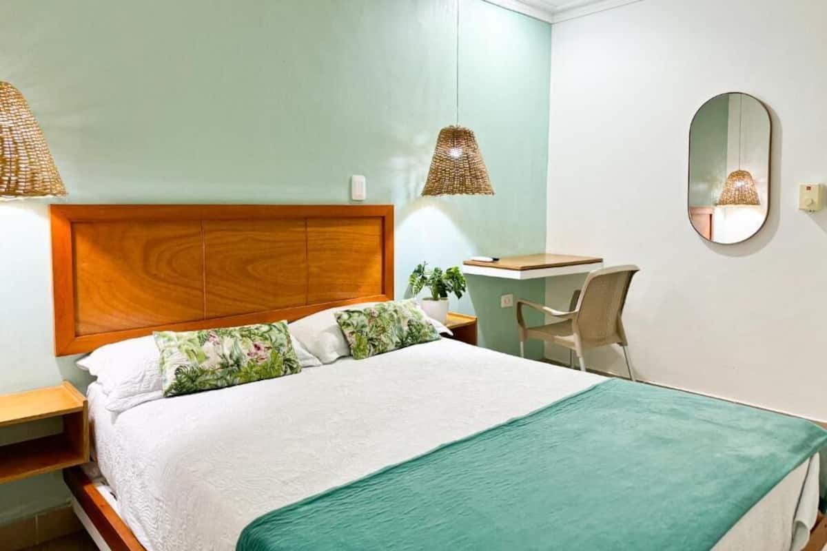 A bedroom with a bed, a desk, a chair, a mirror, and two hanging lamps.