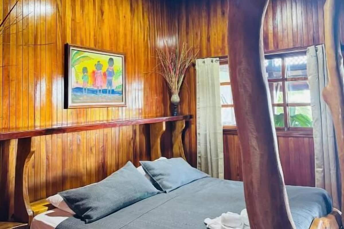 Una habitación de madera con una cama, un cuadro y una ventana.