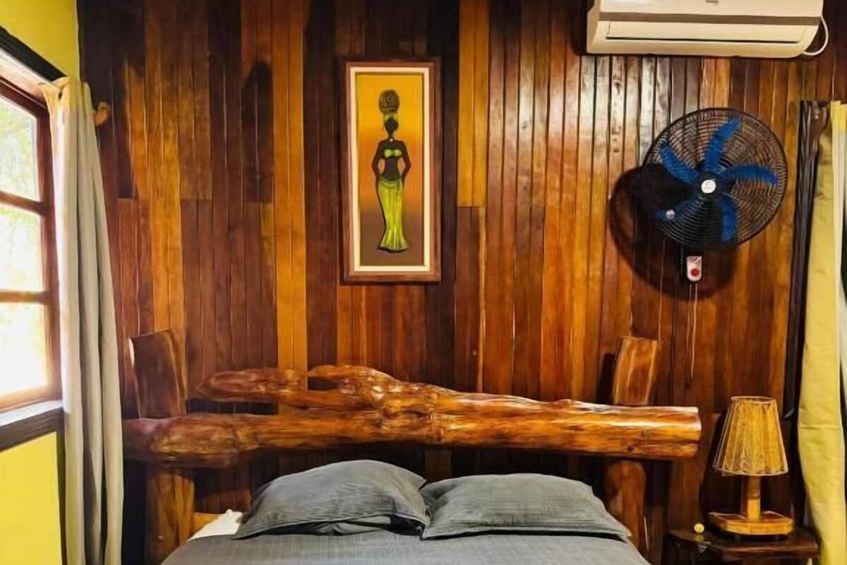 Una habitación de madera con una cama, un ventilador, una lámpara y un cuadro en la pared.