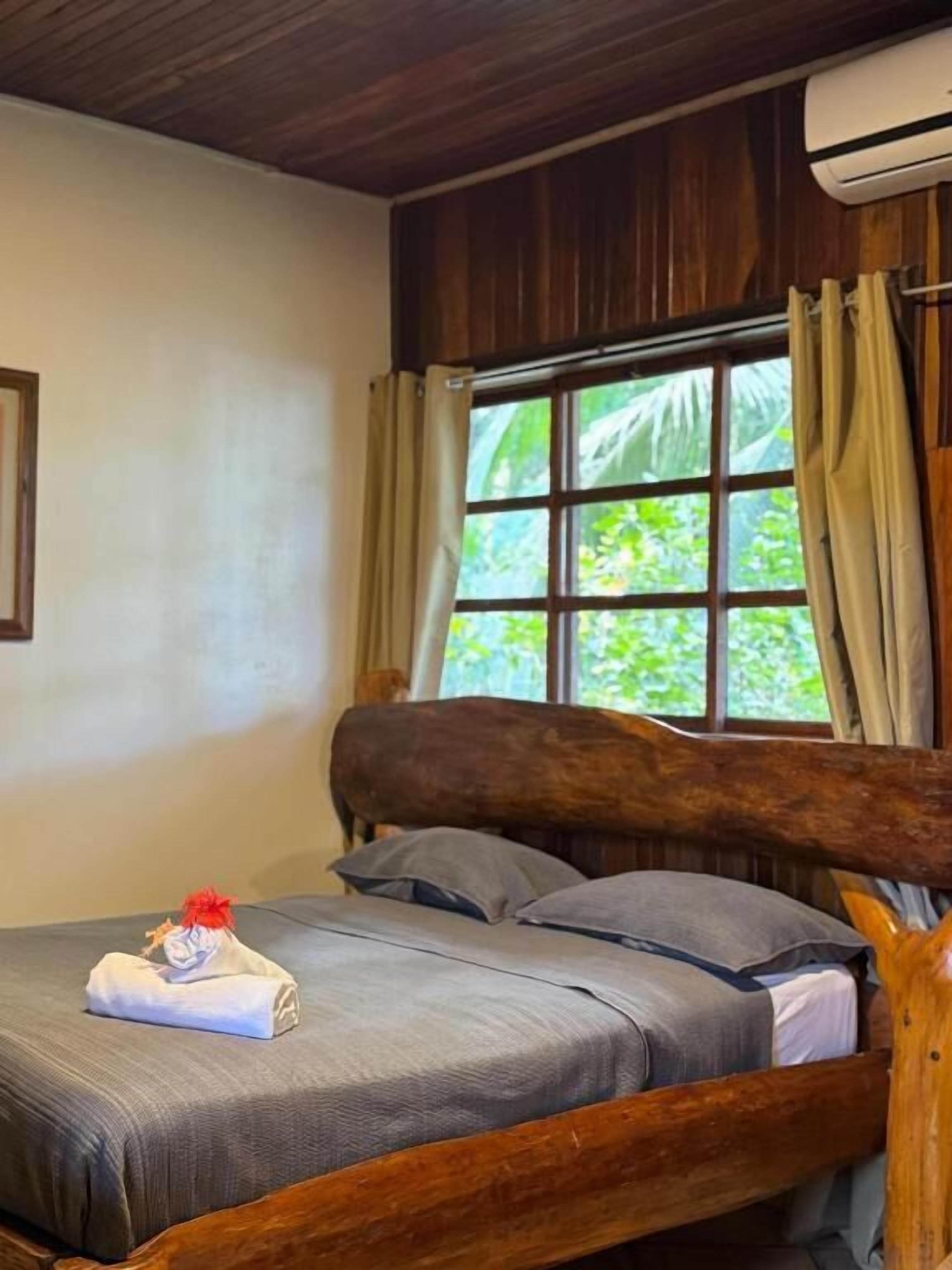A bed with a wooden headboard, a window with curtains, and an air conditioning unit.