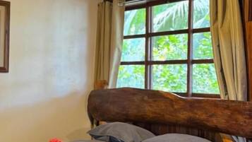 A bed with a wooden headboard, a window with curtains, and an air conditioning unit.