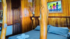 Una habitación con una cama, pilares de madera, un cuadro y un jarrón con ramas.