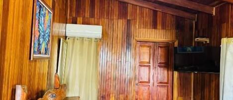 A wooden room with a bed, a wooden headboard, a small table, a door, and a television.