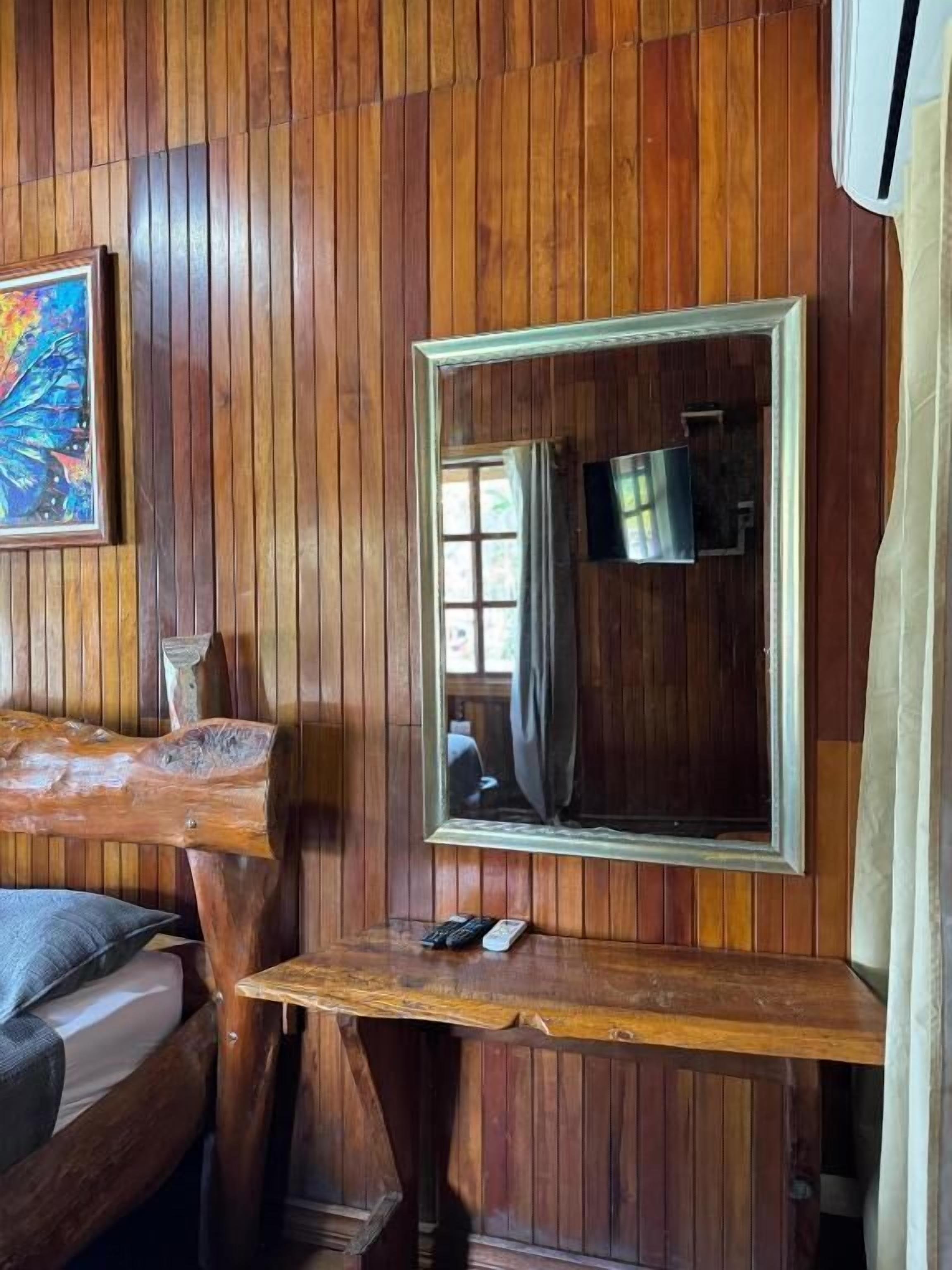 A wooden-paneled room with a bed, a mirror, a television, and a small table with a remote control.