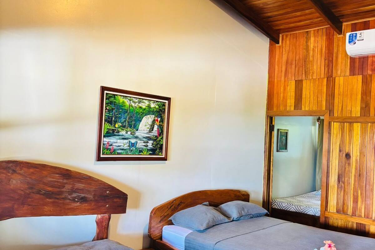 Una habitación con dos camas de madera, un cuadro enmarcados y un espejo en la pared.