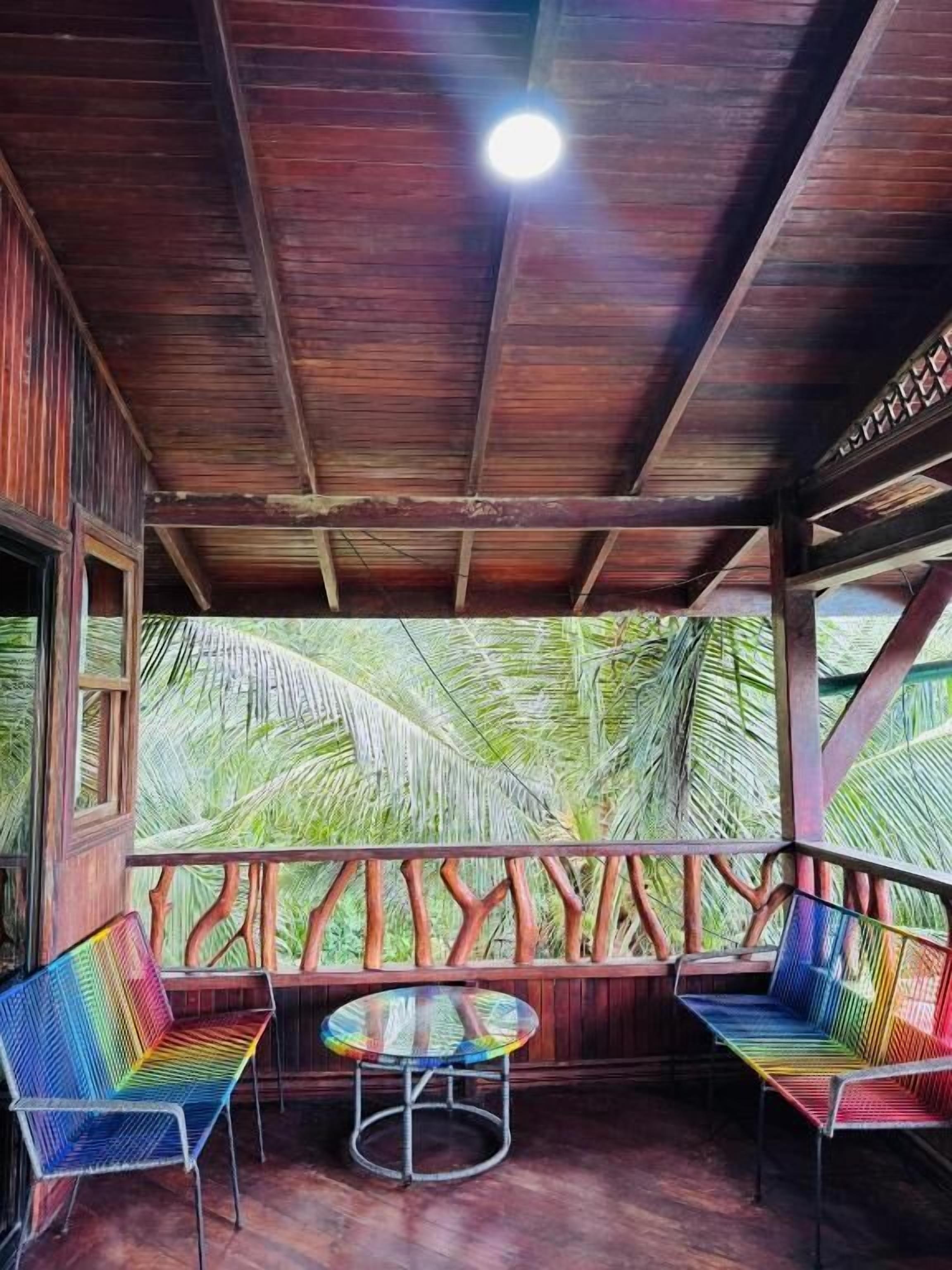 A covered outdoor seating area with wooden beams, two colorful chairs, and a round table.