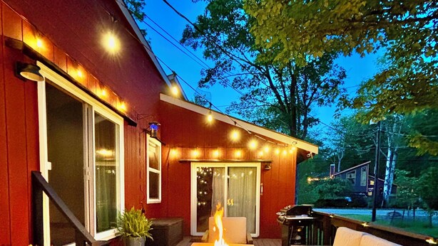 An outdoor patio with a fire feature, seating, and a red building in the background. - Hot Tub in the Poconos -Borders State Forest! (Tobyhanna)
