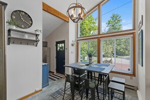 Un coin repas comprenant une table, des chaises, une horloge et une fenêtre donnant sur des arbres.