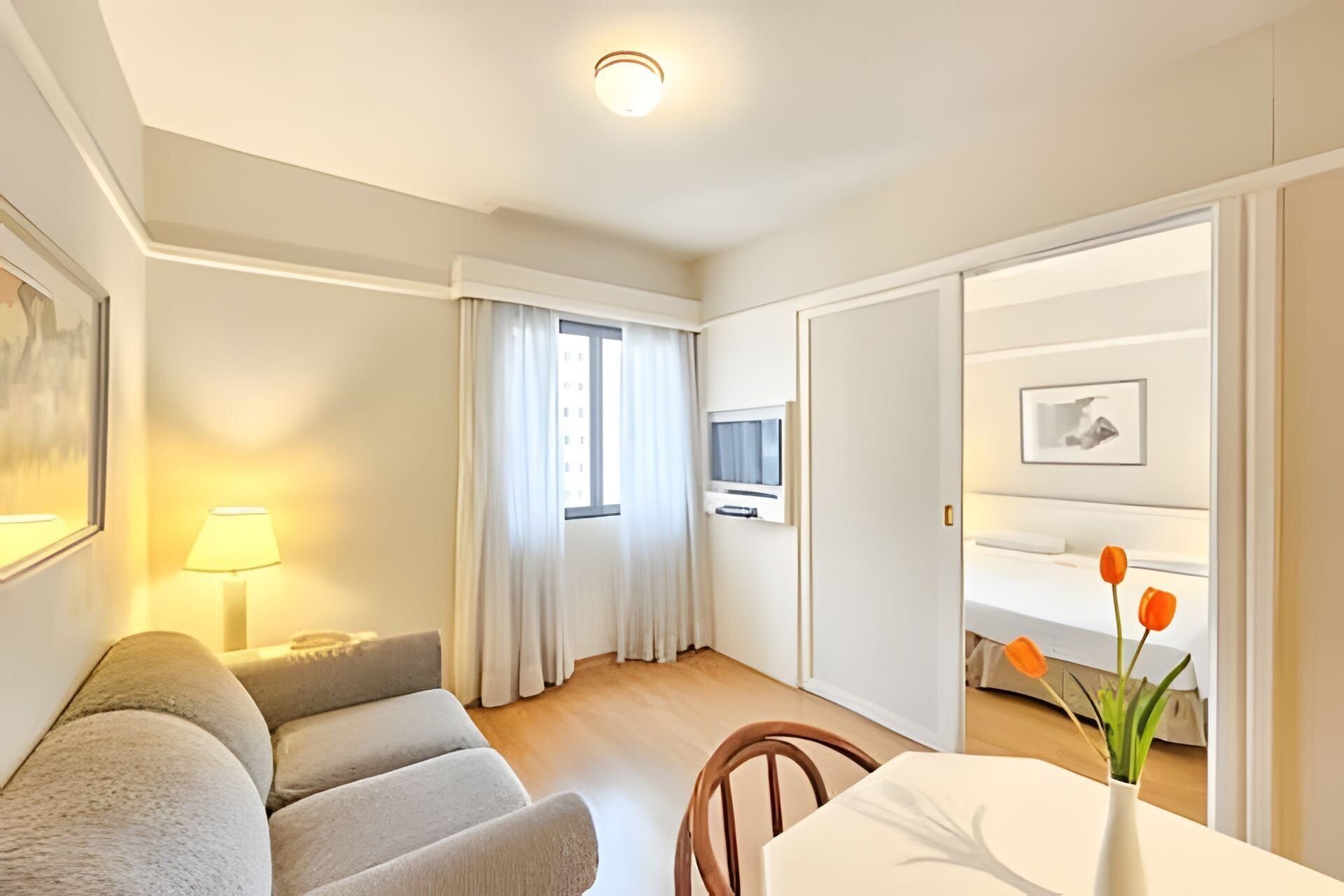 Ein Hotelzimmer mit einer Couch, einem Tisch mit Blumenvase, einem Fernseher und einem Bett mit Fenster.