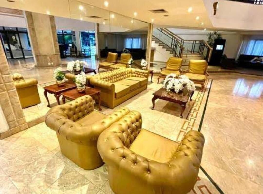 Un vestíbulo amplio con una zona de estar que incluye sofás y sillones capitonados, una escalera y un espejo grande que refleja el interior.