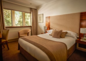 A hotel room with a large bed, two chairs, a nightstand, a lamp, and a window with curtains.