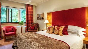 A hotel room with a large bed, a red upholstered armchair, a small round table with a lamp, and a window with curtains. - Knights Suite Rooms and Events (Royal Leamington Spa)